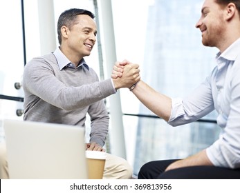 two caucasian teammates coworkers celebrating partnership and success by holding hands in office.