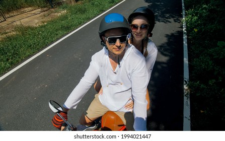 Two caucasian tourist woman man drive on red scooter. Make it selfie. Love couple on motorbike in white clothes to go on forest road trail trip.