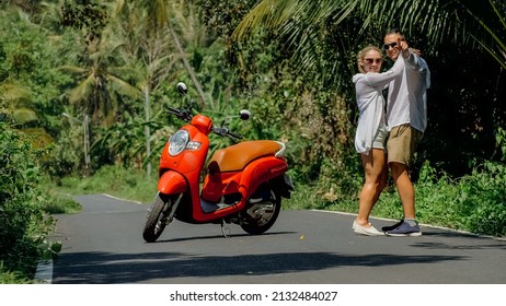 Two Caucasian Tourist Woman Man Dance Near Scooter. Love Couple On Red Motorbike In White Clothes, Sunglasses On Forest Road Trail Trip. Dancing Road. Motorcycle Rent. Asia Thailand Ride Tourism.