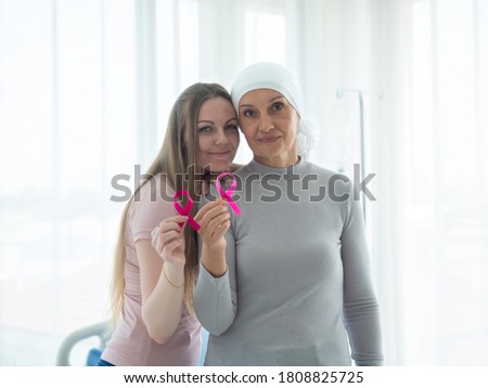Two Caucasian women holding pink ribbon for Cancer awareness. Senior mother with head scarf on standing next to young dauhgter.  Family support.