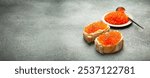 Two caviar toasts baguette canape with butter and red salmon caviar top view on grey concrete background, festive luxury delicacy and appetizer. Space for text