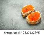 Two caviar toasts baguette canape with butter and red salmon caviar top view on grey concrete background, festive luxury delicacy and appetizer. Space for text