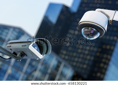 two cctv security camera in a city with blury business building on background