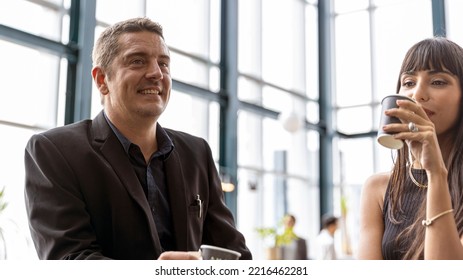 Two CEOs Have A Conversation Over A Coffee Bar With Cityscape Background. A Smart Couple Stand Next To A Bar Counter In An Open Space. Male And Female Managers In Black Dress For Formal Dinner.