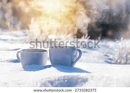 Two ceramic cups with hot coffee standing in fresh snow, steam rising in golden morning light. Cozy winter concept with copy space. Bavaria, Germany.