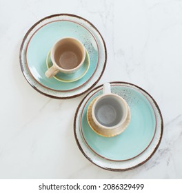 two ceramic cups and plates on white marble table