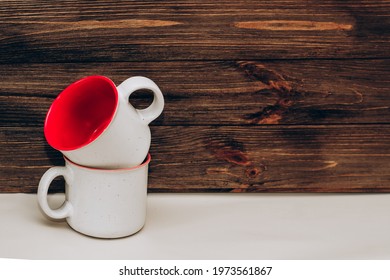 Two ceramic light mugs, inside red on a background of wooden boards.