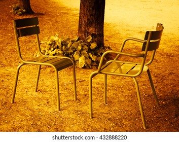 Two chairs facing each other in Tuileries garden. Paris (France). Golden sunset light. Toned photo.