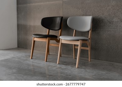 Two chairs in loft interior. A pair of wooden chairs with black and grey seat cushions on concrete floor near grey-brown wall. 