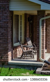 Two Chairs On A Sunny Front Porch Of A Brick House, Next To A Window And Front Door