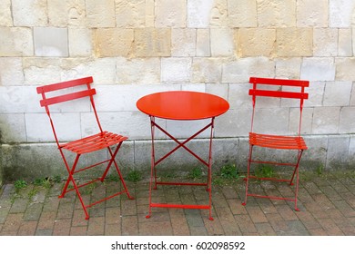 Two chairs and a red table in front of gray a stone wall