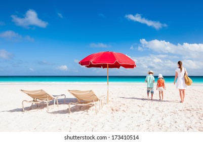 Two Chairs Under Umbrella On A Beautiful Tropical Beach With Family Walking Nearby