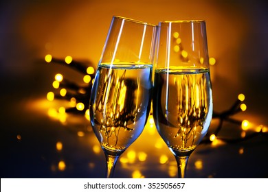 Two champagne flutes clink glasses at Christmas or New Year's  party, warm golden background with blurred lights and copy space
