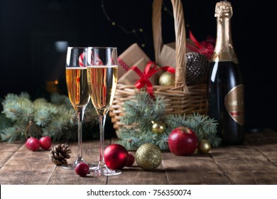 Two champagne glasses and christmas basket bottle, gifts with red satin ribbon, apples candy canes, pine cones branches, golden ornaments garlands on black wall background new year celebration concept - Powered by Shutterstock