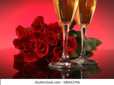 Two Champagne Glasses With A Dozen Red Roses In Background 