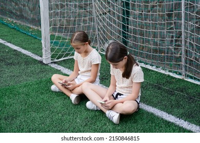 two charming teenage girls in identical clothes with smartphones outside. kids surf the net. smartphone addiction. children in social networks. texting, playing, communicate. - Shutterstock ID 2150846815