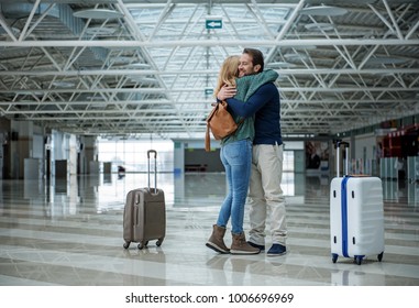 Two cheerful adults hugging each other before departure while standing in the terminal. Suitcases are apart of them - Powered by Shutterstock