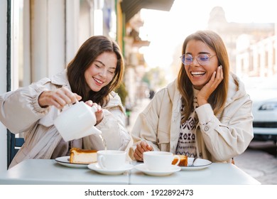 Two cheerful attractive women friends having tea and cakes at the cafe outdoors - Powered by Shutterstock