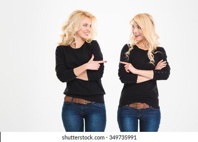Two cheerful attrative sisters twins pointing and looking at each other over white background