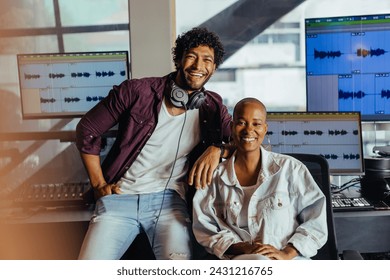 Two cheerful audio professionals pose in a modern recording studio. They are surrounded by sound editing equipment and display screens showing audio waveforms. - Powered by Shutterstock