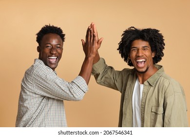 Two Cheerful Black Guys Giving High Five To Each Other, Positive Millennial African American Friends Celebrating Something, Laughing And Having Fun Together Over Beige Studio Background, Copy Space