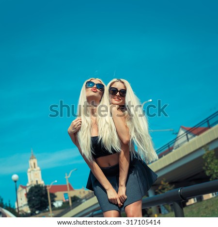 two cheerful blonde girlfriends having fun and fooling around on the street in the city. Two lovely girl friends hugging and having fun.