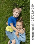 Two cheerful boys are lying on grass, hugging each other. concept of friendship, happy relationship between brothers. Active recreation in park or in school yard. positive, joy of childhood. Top view