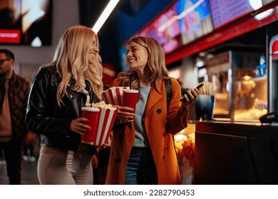 Two cheerful Caucasian girls are in the movie theater having a nigh out, holding tickets, popcorn and beverages in their hands. - Powered by Shutterstock