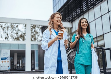 Two cheerful Caucasian women in healthcare attire, a doctor and nurse, walk and converse outside a medical facility, exuding relaxation after a workday. - Powered by Shutterstock