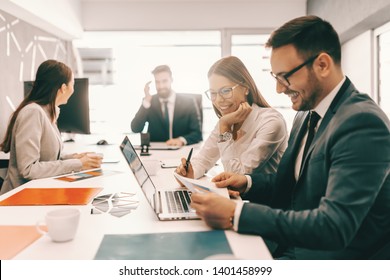 Two Cheerful Colleagues In Formal Wear Solving Problem And Looking At Paperwork. In Background Employees Talking. It Is Literally True That Succeed Best And Quickest By Helping Others To Succeed.