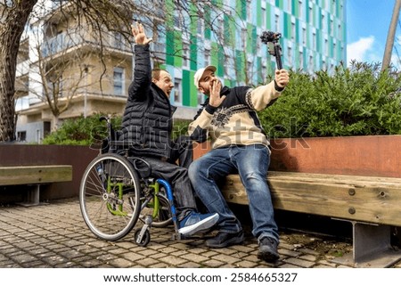 Two cheerful content creators, one in a wheelchair, are recording a video blog in an urban setting, using a gimbal for stabilized footage