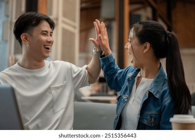 Two cheerful and excited young Asian friends are celebrating good news together, giving each other a high five with overjoyed expressions. teamwork, friendship, colleague, best friend - Powered by Shutterstock