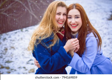 Two cheerful girls best friends, in the street. Portrait young pretty womans friends in friendly hug. Walking at the city. Wearing stylish outerwear and hats. Bright make up. Positive emotions. Cuties