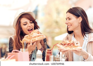 Two cheerful  girls eating pizza in a outdoor cafe.