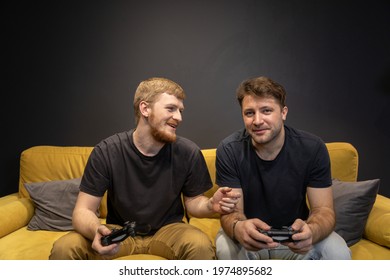 two cheerful handsome guys passionately Playing Videogame together in modern living-room interior lifestyle. Crazy Male gamers Couple gaming concept. Hobby Resting At Home on yellow sofa copy space