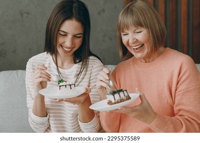 Two cheerful happy adult women mature mom young kid wearing casual clothes eat sweet yummy cake sit on gray sofa couch stay at home flat rest relax spend free spare time in living room. Family concept - Powered by Shutterstock