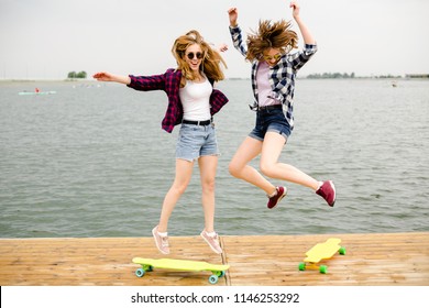 Two cheerful happy skater girls in hipster outfit having fun on a wooden pier during summer vacation - Powered by Shutterstock