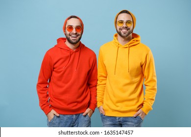 Two cheerful hipster men guys in fashion red yellow clothes eyeglasses posing isolated on pastel blue background studio portrait. People emotions lifestyle concept. Mock up copy space. Looking camera - Powered by Shutterstock