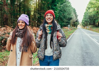 Two cheerful hitchhiker female traveler walking on the roadside with backpack. Two smiling beautiful caucasian sisters hiking on an empty highway. Tourism and travel concept. - Powered by Shutterstock