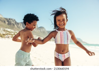 Two cheerful little kids having fun and enjoying themselves at the beach. Two adorable ethnic kids smiling happily while playing around in swimwear.