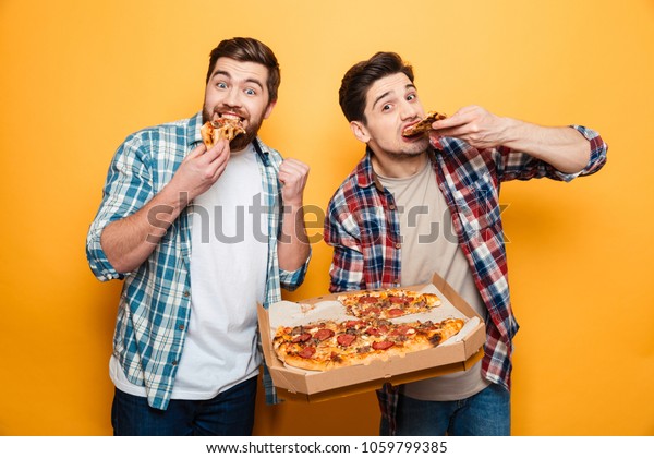 シャツを着た2人の明るい男性がピザを食べ 黄色い背景にカメラを見る の写真素材 今すぐ編集