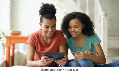 Two Cheerful Mixed Race Curly Girlfriends Shopping Online With Tablet Computer And Credit Card At Home