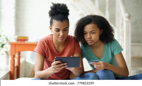 Two Cheerful Mixed Race Curly Girlfriends Shopping Online With Tablet Computer And Credit Card At Home