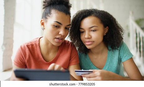 Two Cheerful Mixed Race Curly Girlfriends Shopping Online With Tablet Computer And Credit Card At Home