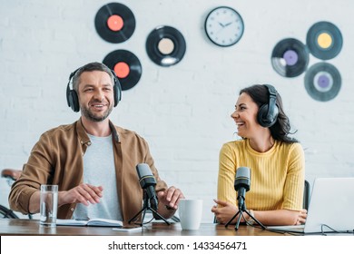 two cheerful radio hosts in headphones recording podcast in studio together - Powered by Shutterstock