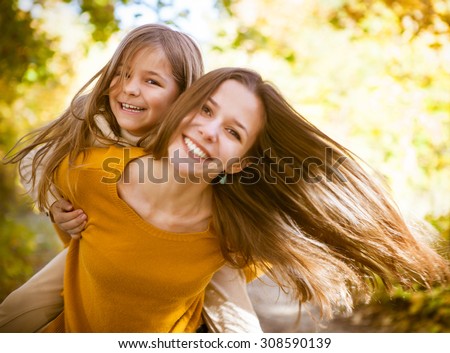 Two cheerful sisters playing in the park in warm autumn day