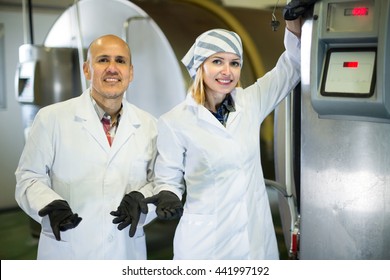 Two cheerful smiling farm workers operating modern fresh milk cooling system in plant