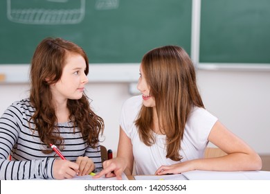 Two Cheerful Students Talking While Writing Notes In School Room