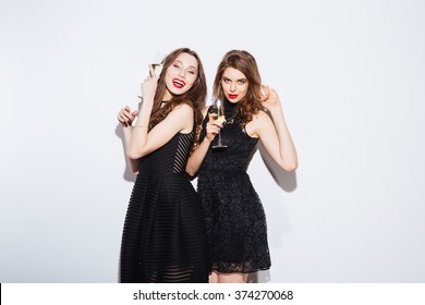 Two cheerful women posing in night dress with glass of champagne isolated on a white background