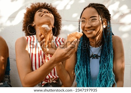 Two cheerful young african american women sharing ice cream while spending time together outdoors on sunny day